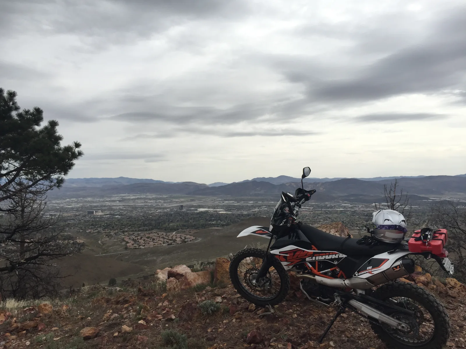 Black and white KTM enduro motorcycle parked on a rocky overlook above a valley.