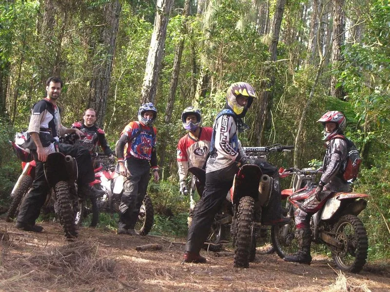 Group of riders and dirt bikes paused together on a wooded trail.