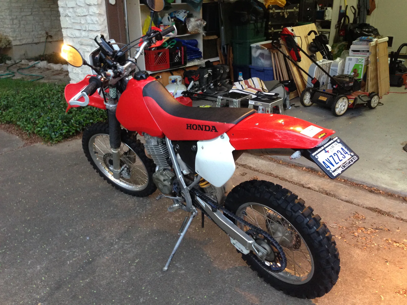 Red Honda dual-sport motorcycle parked outside a garage at dusk.