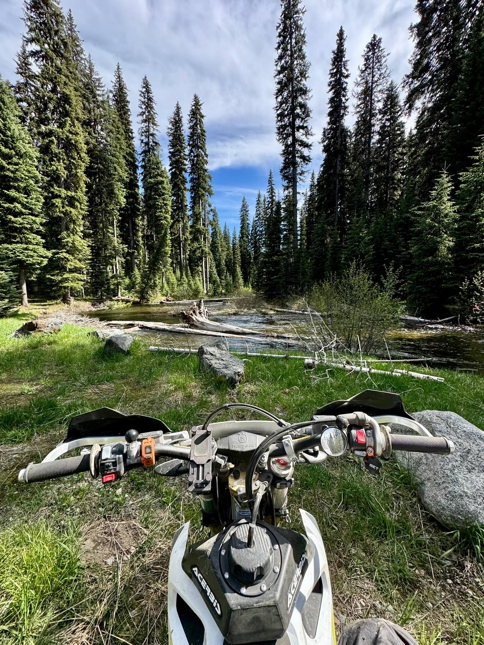 Orange KTM dirt bike at a forest campsite with tents in the background.