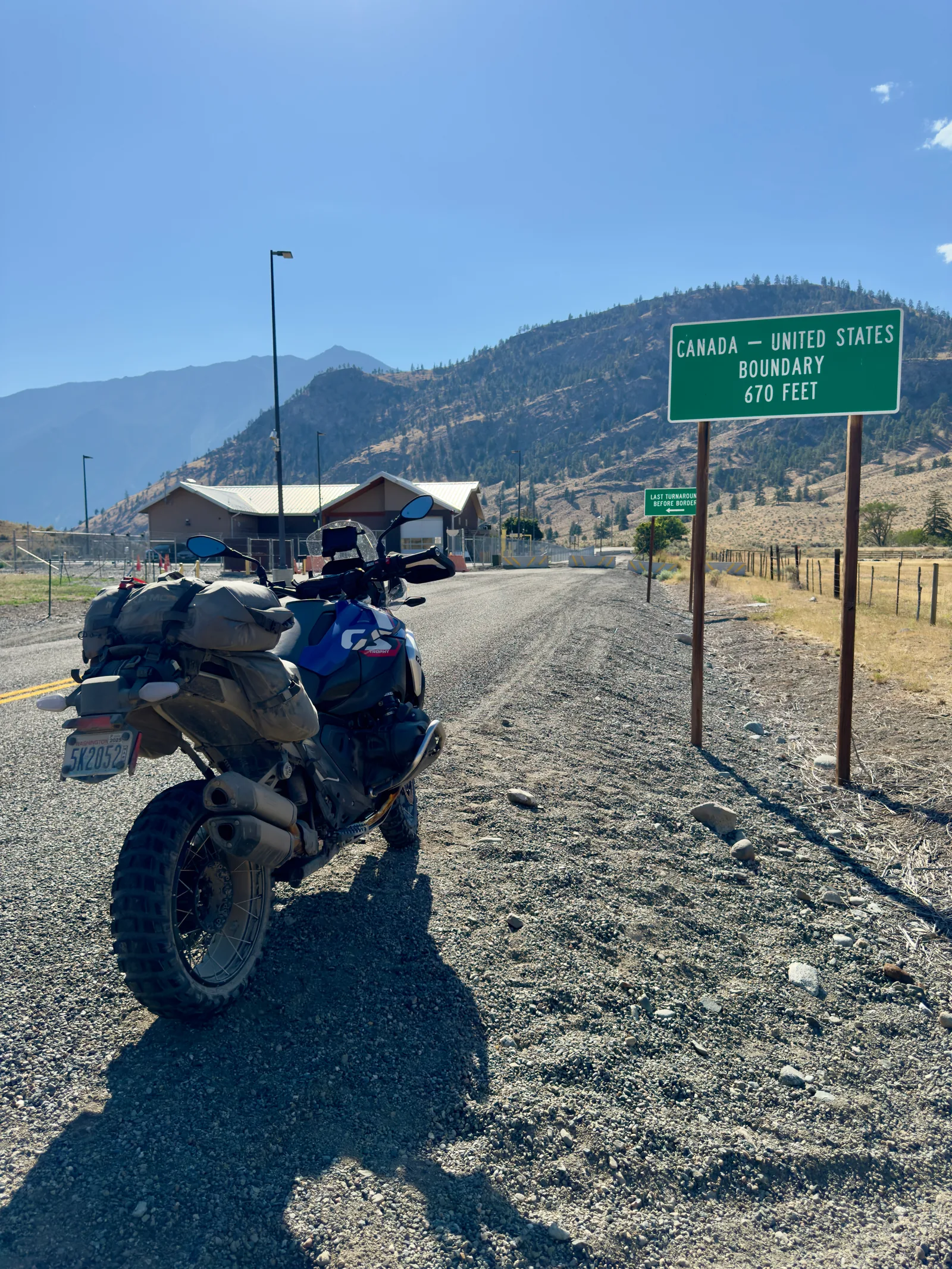 Blue BMW GS motorcycle parked beside a Canada-United States boundary marker.