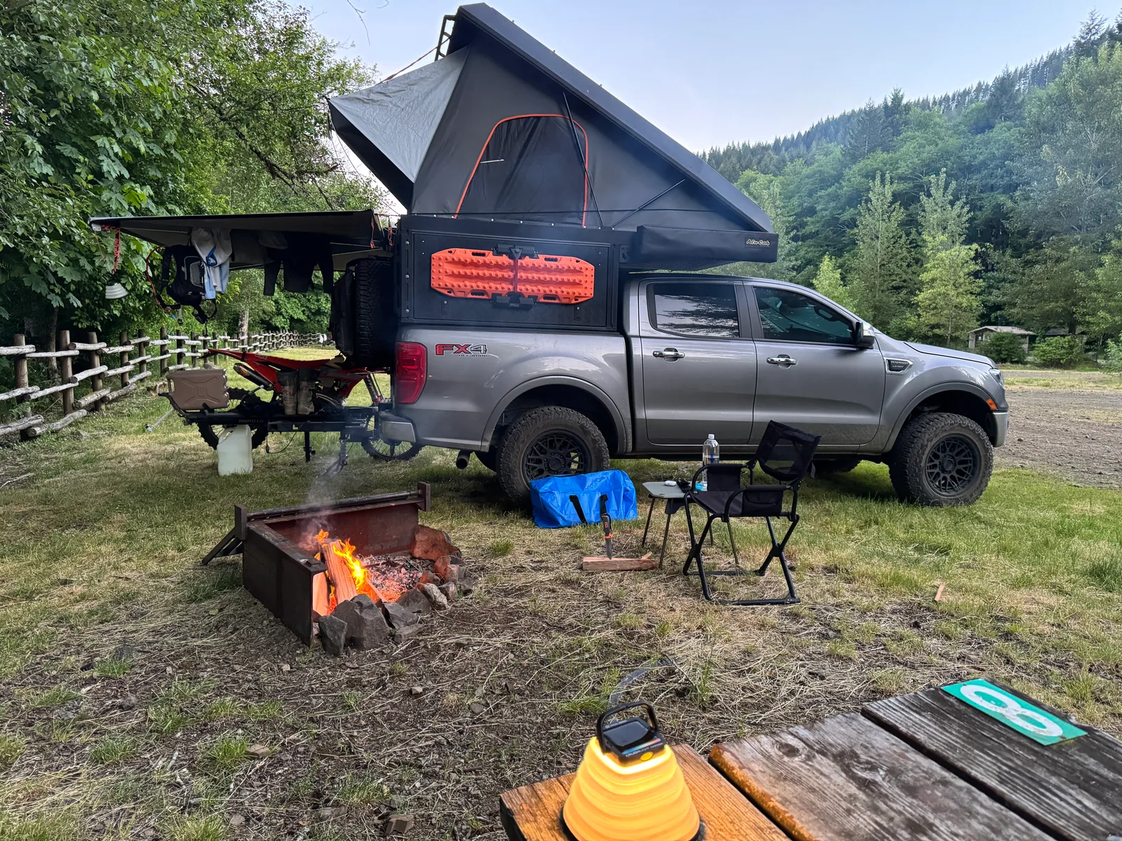 Truck with a rooftop tent at a forest campsite.